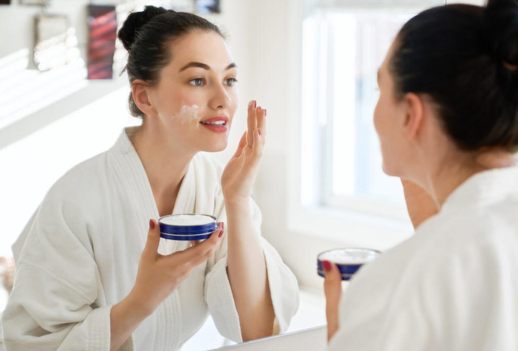 A woman applying cream looking at the mirror